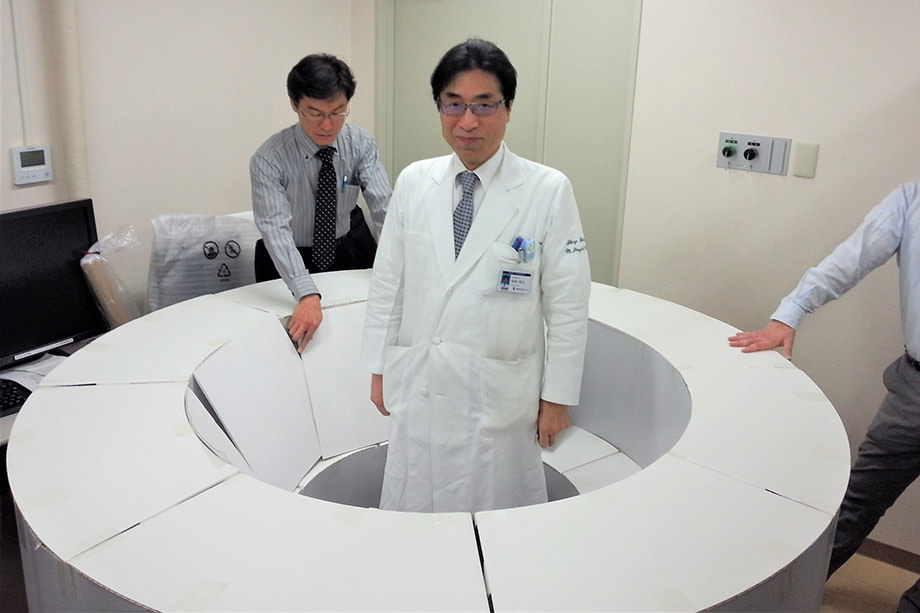 This image shows Professor Jinzaki experiencing the size of the device using a life-size model made of cardboard.