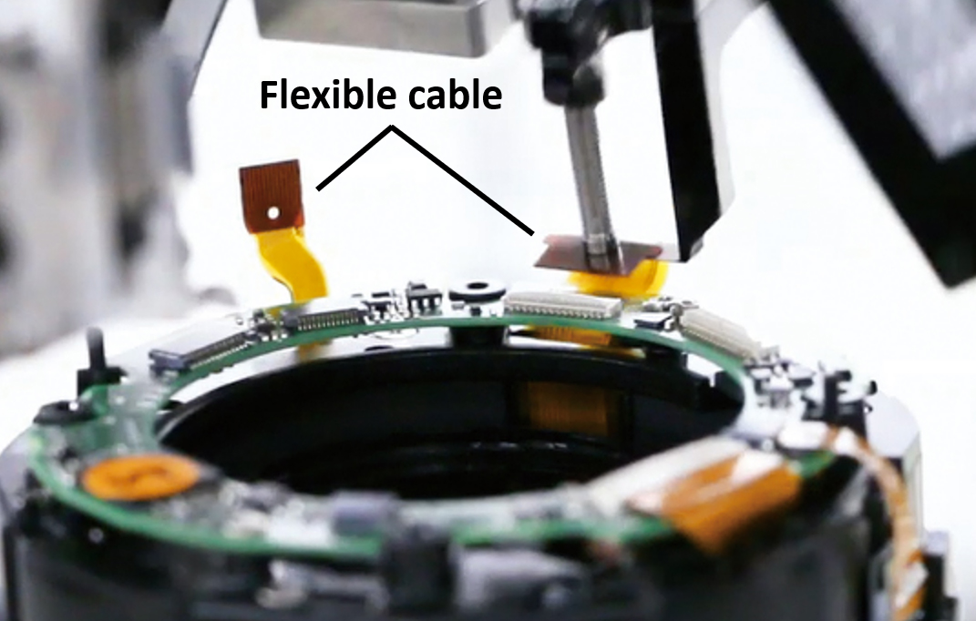 An automated lens production device inserts flexible cables